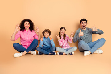 Happy family of four sitting together on a beige background while making playful hand gestures,...