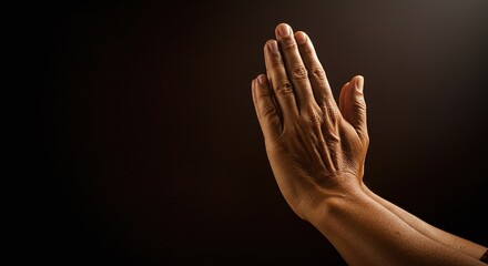 Fototapeta premium An image showing a hand in a prayer pose against a dark background, the skin is textured and a wedding band is visible on the ring finger