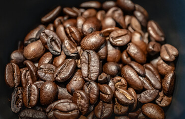 A close-up macro shot of roasted coffee beans, highlighting their rich brown tones, glossy texture, and natural imperfections.