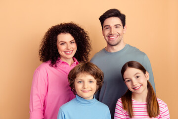 Fototapeta premium Cheerful young family posing together against a beige background, featuring two parents and their cheerful children