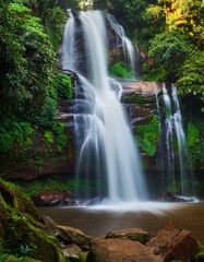 Fototapeta premium Green forest, big trees with green leaves canopy, long exposure of waterfall, ray of light