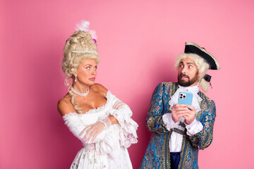 Elegant couple in historical costumes with smartphone against a pink background, depicting vintage aristocratic fashion