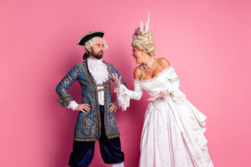 Couple in elaborate royal costumes posing together with expressions against a pink background