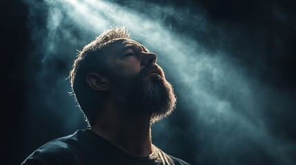 A bearded man looks upwards into rays of bright light