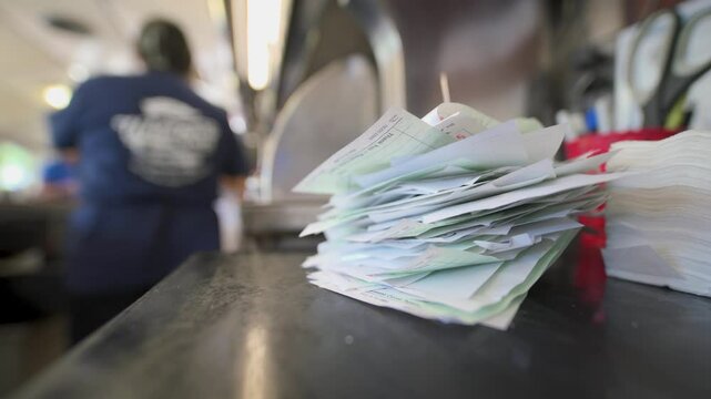 In a busy kitchen environment, order slips are stacked high, indicating a bustling atmosphere