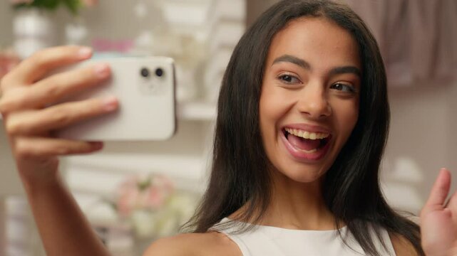 Smiling happy Latina girl Hispanic woman fashion blogger influencer model in bathroom holding mobile phone beauty blog skincare cosmetics makeup tutorial social media content photo selfie video call