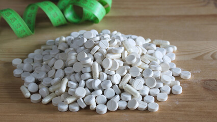 White pills and capsules piled up near green measuring tape representing diet and slimming