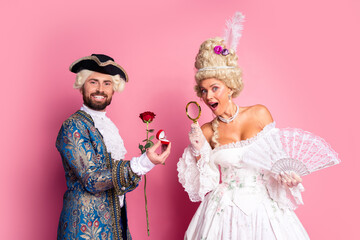 Young couple dressed in vintage royal-themed costumes posing in vibrant expressions on a pink background