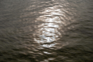 Sunlight reflection on rippling water surface creating abstract pattern. Close-up of shimmering light on lake or river waves.