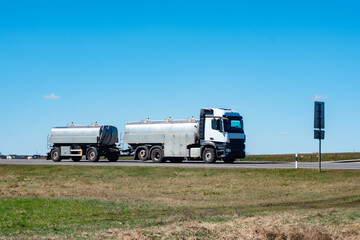 Silver tanker truck travels on a highway under a clear blue sky. Concept logistics of liquid...