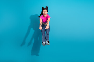 Young woman in stylish casual fashion jumps against a vibrant blue backdrop with excitement and joy