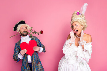 Elegant couple dressed in royal-themed costumes in a playful and romantic mood against a pink background