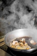 A pan filled with cooking clams releases steam, capturing the essence of seafood preparation in a bustling kitchen, highlighting the beauty of culinary processes.
