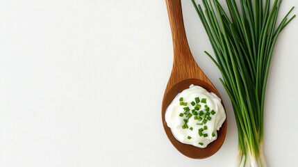 A wooden spoon holds creamy dip garnished with chopped chives, accompanied by fresh green onions on a clean white surface, suggesting a culinary preparation for a gathering