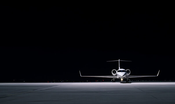 Private jet awaits take-off on the dark runway. Luxury travel and business flights are synonymous with this modern plane on the black airfield.