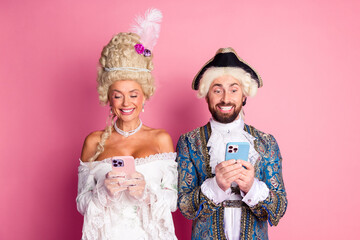Couple in historical costumes enjoying modern technology with stylish pink background