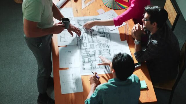 Top view of interior designer planing building while project manager working and holding coffee. Group of engineer brainstorming idea and designing house structure while presenting idea. Symposium.
