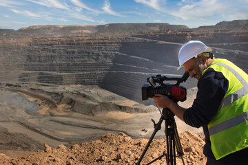 cameraman operating a camera on a tripod, at an open pit mine making a documentary