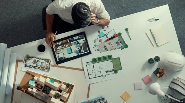 Top view of engineer drink coffee and thinking about house plan at meeting table with equipment and safety helmet scatter around. Aerial view of stressful manager looking at blueprint. Alimentation.
