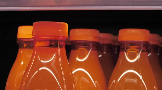Bright orange beverage bottles on store shelf ready for customers to enjoy refreshing juice anytime_j1