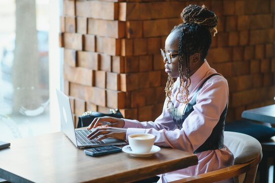 Portrait of smart young woman with mobile phone working on laptop at outdoor coffee shop