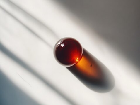Minimalist photo of a single drop of deep red liquid, highlighting its transparency, texture, and reflection on a white background