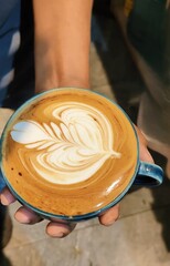 Hand holding a cup of coffee with a flower design.