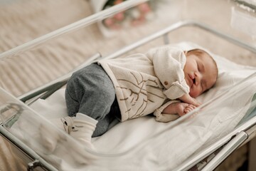 A newborn baby sleeping peacefully in a hospital bassinet, wearing a cozy outfit.