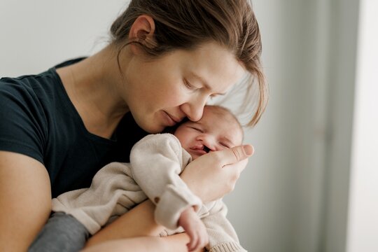 A tender moment between a mother and her newborn baby, with the mother gently kissing the baby's forehead. The baby is wrapped in a soft beige blanket, and the scene conveys warmth and love.