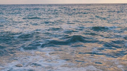 Ocean water with rolling waves on windy day at sunset light slow motion. Azure sea water with small running waves at exotic resort in summer evening. Waves with foam run on beach at wild seaside