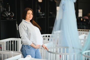 Happy pregnant woman choosing a baby crib in the store