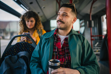 young man go to work hold thermos while riding a bus in the city