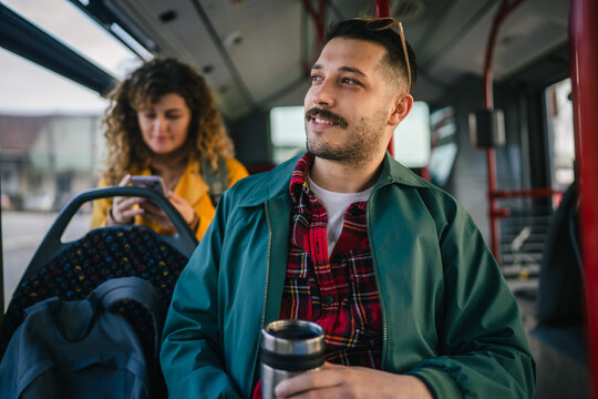 young man go to work hold thermos while riding a bus in the city