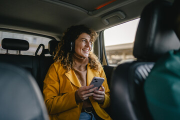 woman with headphones use a mobile phone while ride in a taxi