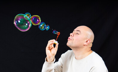 adult bald man blowing soap bubbles. on a black background.