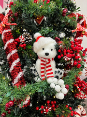 Small teddy bear sits on a Christmas tree decorated with garlands, balls and candies