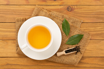 Cup of tea with dry and fresh leaves on wooden background, top view