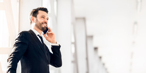 Happy wealthy businessman standing in airport, talking on phone, having business trip, panorama...