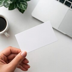 Obraz premium Blank business card mockup held by hand with coffee cup and laptop for branding design 