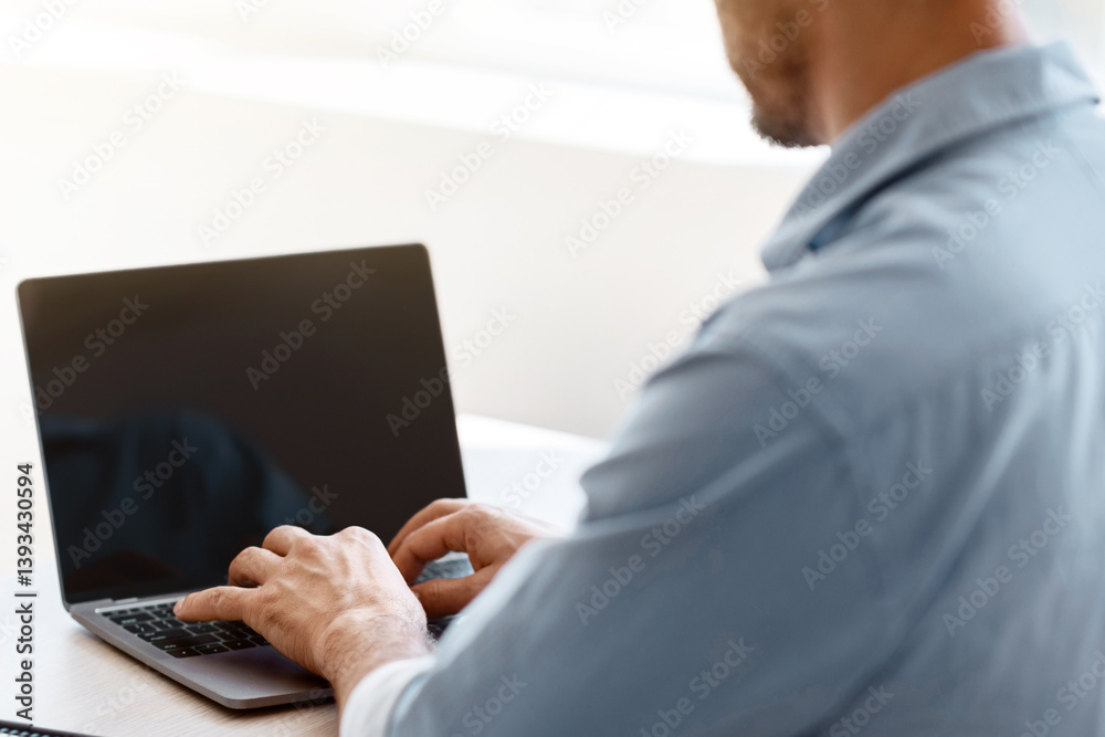 Poster unrecognizable businessman working on laptop with black screen, sitting at desk in office, typing on