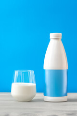 Fresh milk in glass cup and plastic bottle on blue background