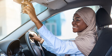 Buying New Car. Muslim African Lady In Hijab Adjusting Rear View Mirror, Testing Auto, Enjoying Her New Vehicle, Sitting On Driver's Seat In Modern Automobile, Side View Shot With Free Space