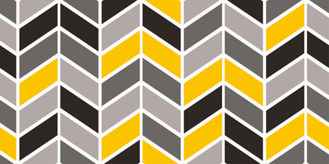 The pattern is composed of black, gray, light gray, and yellow rectangles arranged in a repeating chevron formation. Abstract wall.