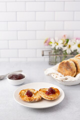 Homemade English Muffin with Butter and Jam on a White Plate with Bowl of English Muffins in Background