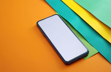 Fototapeta premium Smartphone with blank white screen display lies on orange backdrop with colorful green and yellow sheets. Modern mobile tech, app interface or website mockup.