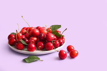 Plate of sweet cherries and leaves on lilac background