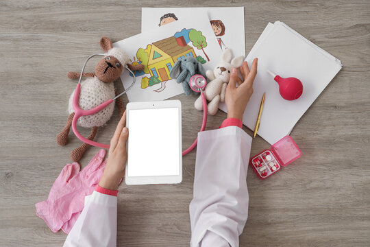 Female doctor hands with tablet computer, toys and pills at grey wooden table