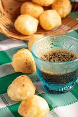 Brazilian cheese bread with coffee, delicious Brazilian cheese bread with a cup of coffee and accessories on a rustic table with a green and white checkered tablecloth, selective focus.