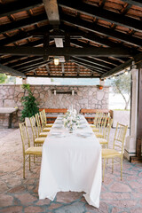 Long covered festive table stands in the garden under a wooden canopy
