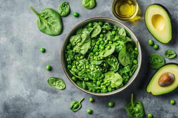 Obraz premium Green spinach and pea salad in a bowl, surrounded by avocado and olive oil on dark stone background.